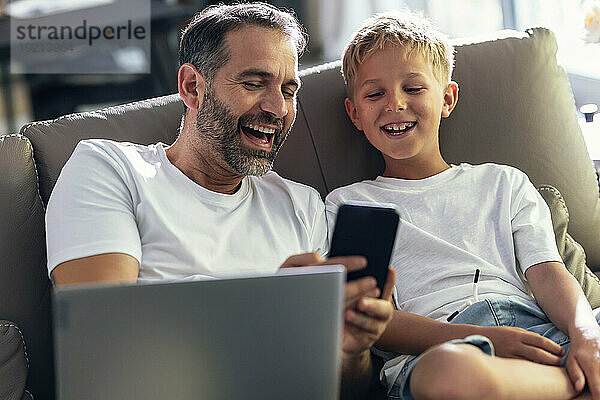 Mann teilt Smartphone und lacht mit Sohn zu Hause