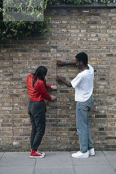 Junger Mann und Frau öffnen Tür in der Nähe einer Ziegelmauer