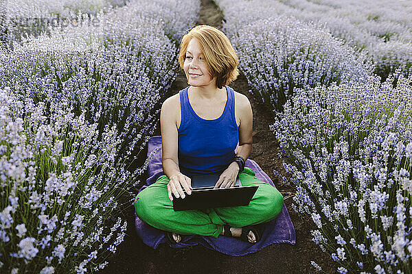 Glückliche Frau sitzt mit gekreuzten Beinen inmitten eines Lavendelfeldes