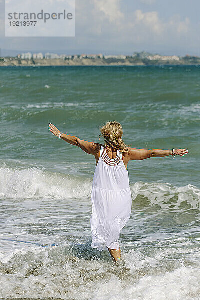 Carefree woman with arms outstretched walking in sea at beach