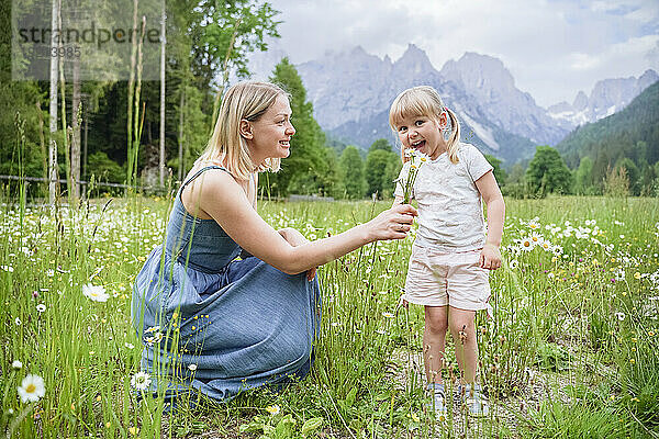Lächelnde Frau schenkt ihrer Tochter  die inmitten von Pflanzen steht  einen Strauß Gänseblümchen