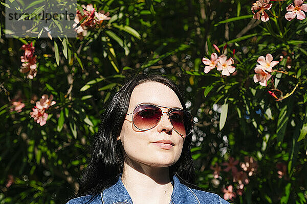 Junge Frau mit Sonnenbrille in der Nähe blühender Pflanzen an einem sonnigen Tag