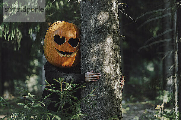 Frau trägt Jack O' Lantern und umarmt Baum im Wald