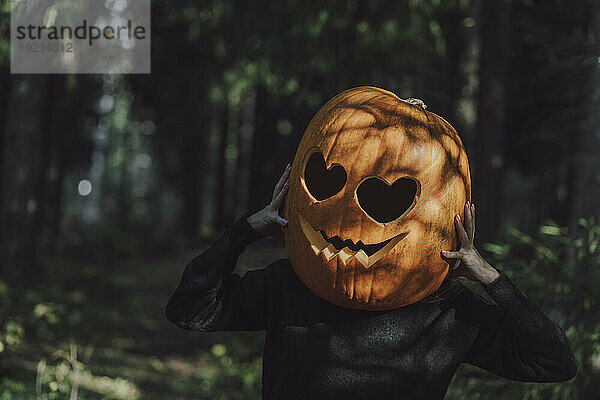 Frau hält Jack O‘Lantern im Wald übers Gesicht