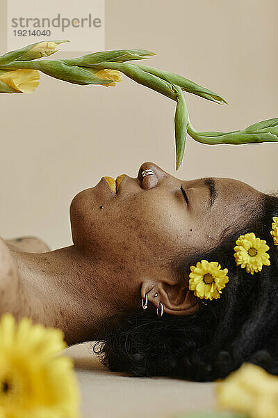Junge Frau mit gelben Blumen im Haar entspannt sich vor braunem Hintergrund