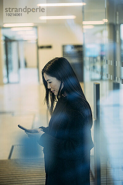 Businesswoman using smart phone standing in workplace