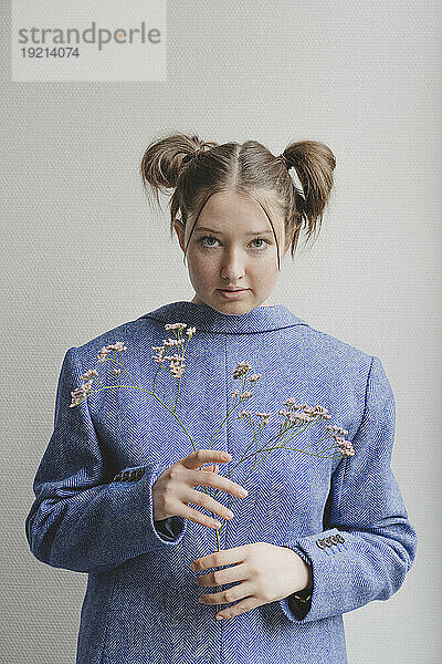 Teenagermädchen trägt blauen Blazer verkehrt herum und hält Blumen vor der Wand