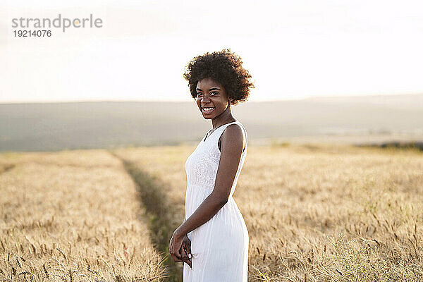 Glückliche junge Frau  die bei Sonnenuntergang im Weizenfeld steht