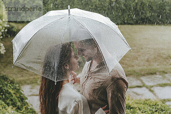 Romantic couple standing with umbrella in rain at garden