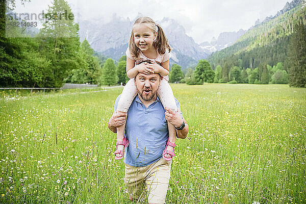 Verspielter Mann  der seine Tochter auf den Schultern trägt und vor den Bergen spaziert