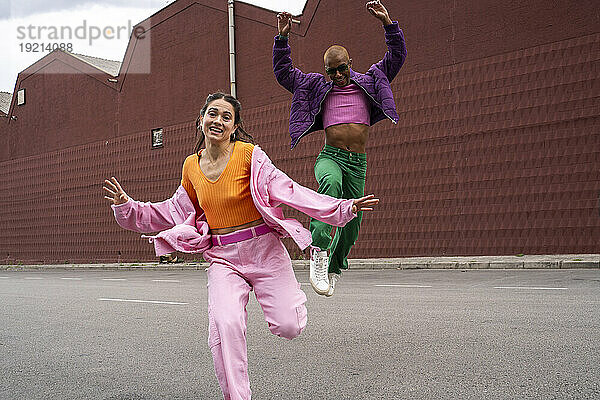 Fröhliche Frau tanzt mit Freundin und springt vor Gebäude