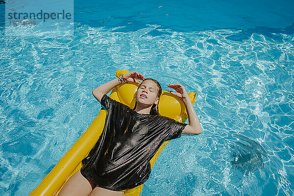 Girl with eyes closed relaxing on pool raft at sunny day