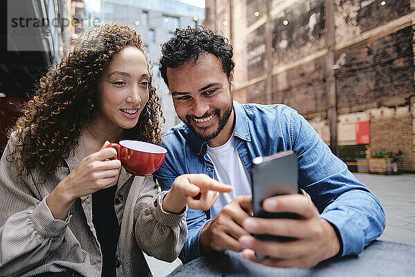 Glücklicher Mann und Frau  die ihr Smartphone im Straßencafé benutzen