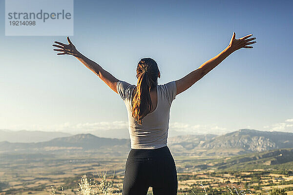 Young woman with arms outstretched standing in front of sky