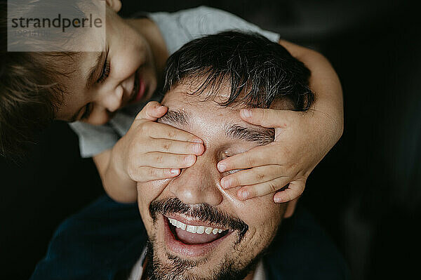 Smiling son covering father's eyes