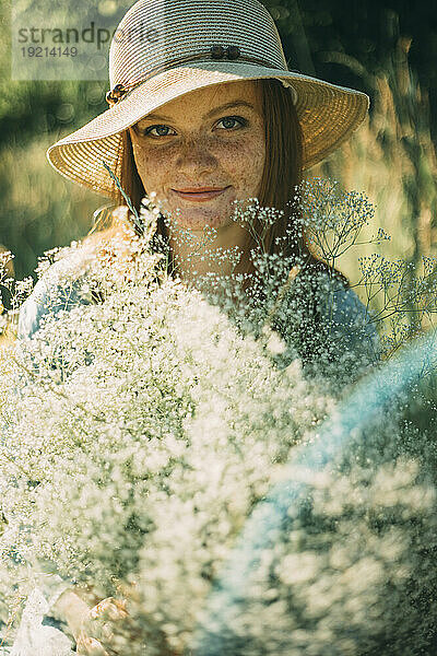 Lächelnde junge Frau mit Blumen an einem sonnigen Tag