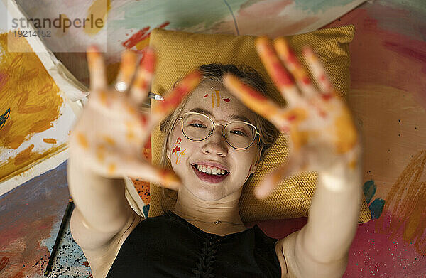 Lächelnde Frau zeigt Handflächen  die auf Gemälden liegen