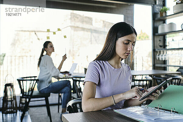 Portrait of pretty brunette using digital tablet at table in coworking office