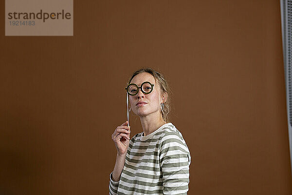 Selbstbewusste Frau mit Brillenstütze vor braunem Hintergrund