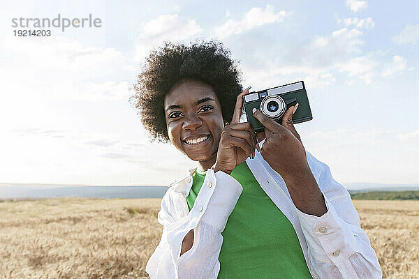 Smiling young woman holding camera in field