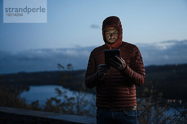 Reifer Mann benutzt Tablet-PC in der Abenddämmerung unter Himmel