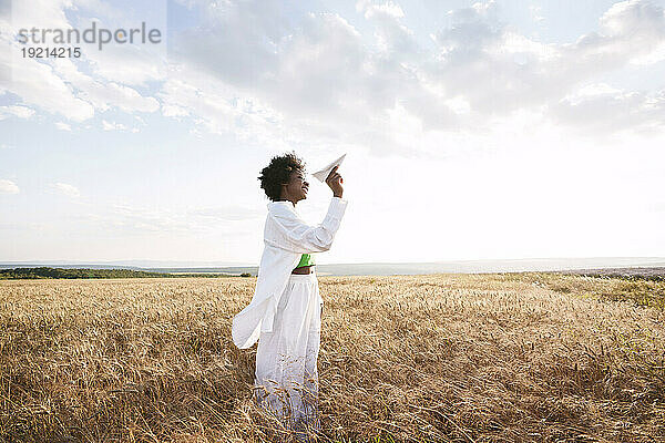 Frau spielt mit Papierflieger und steht auf dem Feld