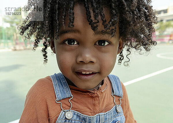 Lächelnder Junge mit lockigem Haar auf dem Basketballplatz