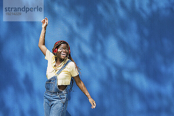 Glückliche junge Frau tanzt vor einer blauen Wand
