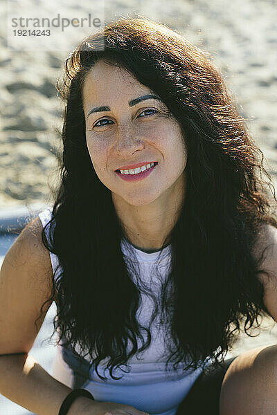 Glückliche Frau mit langen schwarzen Haaren am Strand an einem sonnigen Tag