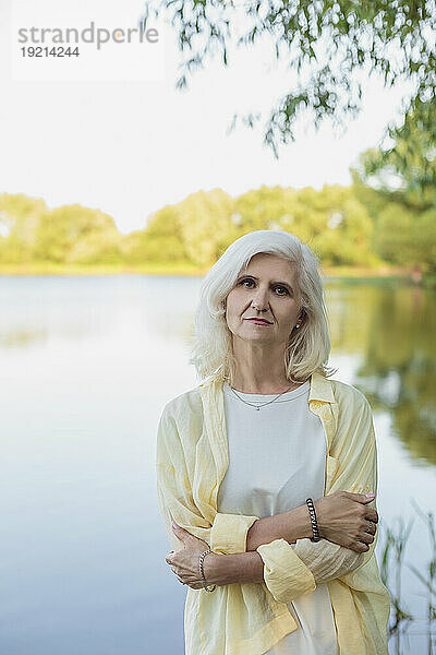 Reife Frau mit weißem Haar umarmt sich vor dem See