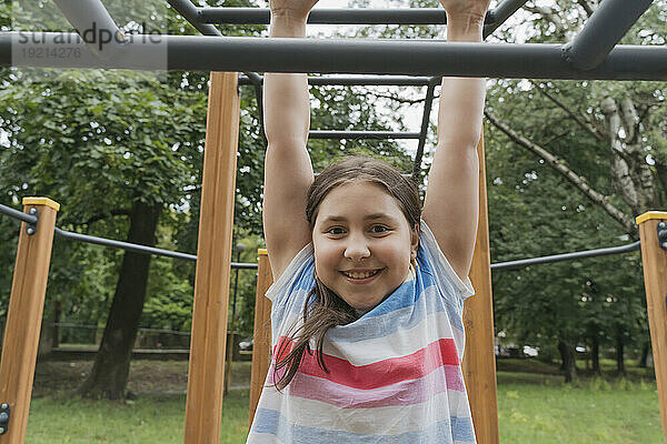 Lächelndes Mädchen hängt am Klettergerüst auf dem Spielplatz