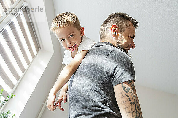 Playful father carrying son on shoulder at home
