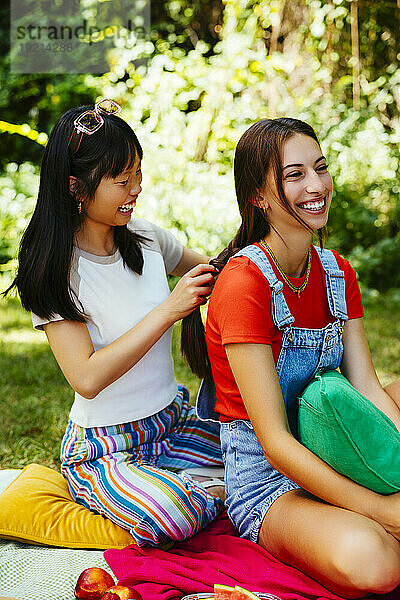 Smiling woman braiding friend's hair in garden
