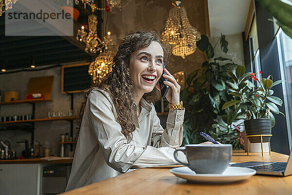 Glückliche Geschäftsfrau  die im Café sitzt und mit dem Handy spricht