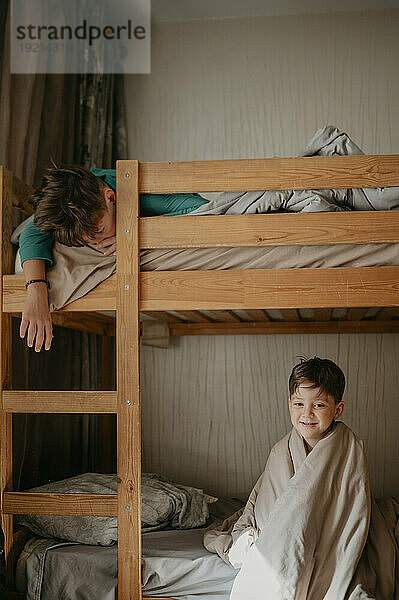 Lächelnder Junge sitzt mit seinem Bruder auf einem Etagenbett