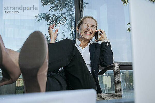 Glückliche Geschäftsfrau  die auf einem Stuhl sitzt und über ihr Mobiltelefon spricht