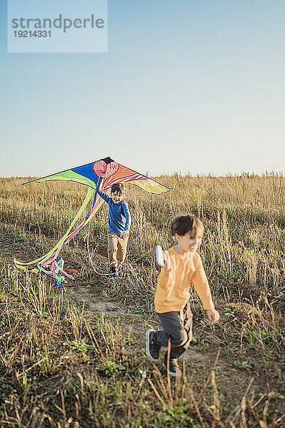 Happy brothers playing with kite in field under sky