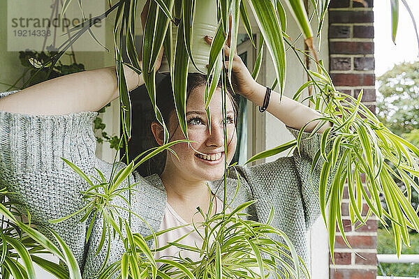 Glückliches Teenager-Mädchen trägt eine eingetopfte Spinnenpflanze auf dem Kopf auf dem Balkon