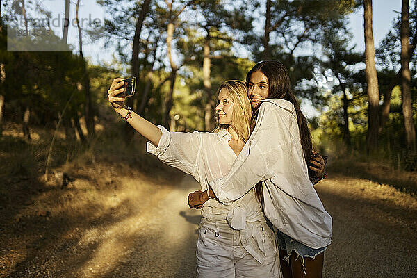 Frau macht Selfie mit Teenager-Tochter  die sie im Wald umarmt