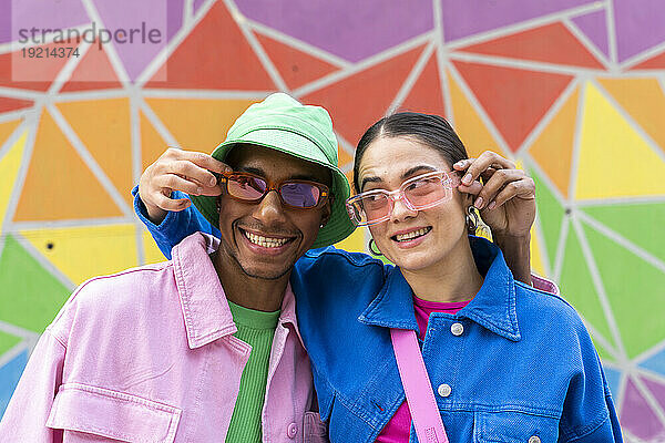 Smiling couple holding sunglasses in front of colorful wall