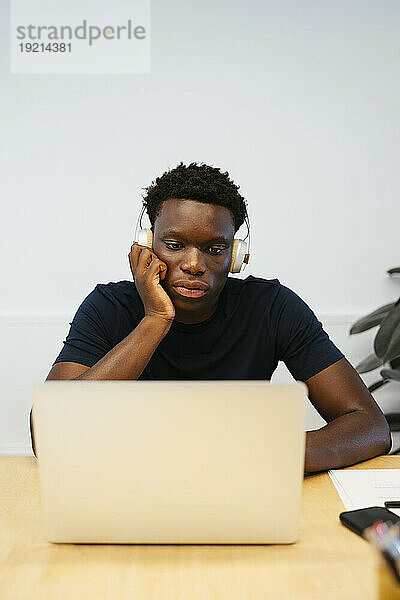Student trägt kabellose Kopfhörer und benutzt Laptop am Schreibtisch