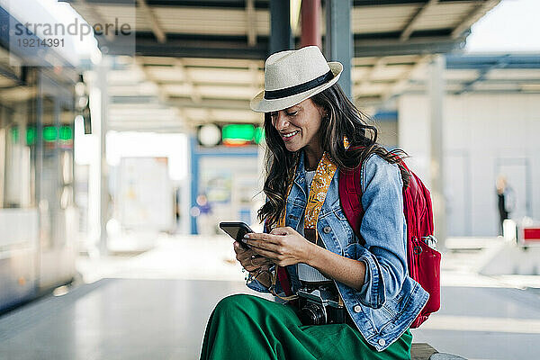 Glückliche Frau  die ihr Mobiltelefon an der Straßenbahnhaltestelle benutzt