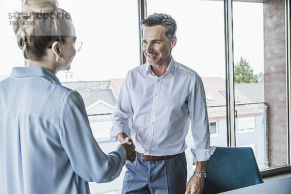 Smiling businessman shaking hands with businesswoman in office