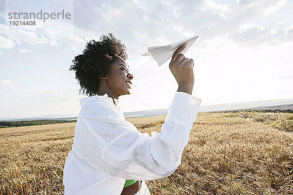 Glückliche Frau mit lockigem Haar hält Papierflieger im Feld