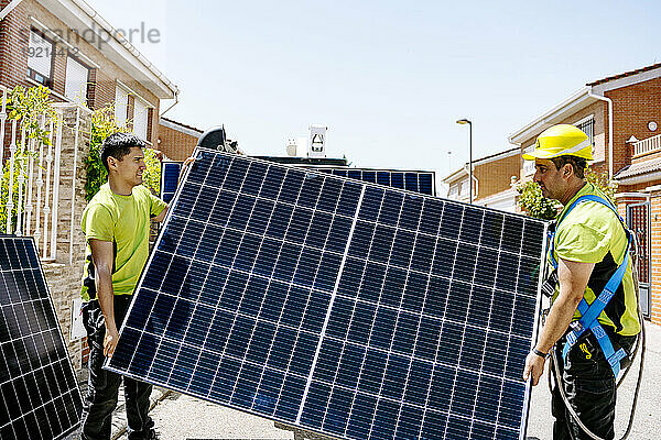 Ingenieur trägt Solarpanel mit Kollegen an sonnigem Tag