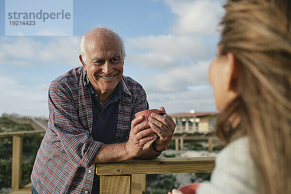 Glücklicher älterer Mann hält eine Kaffeetasse in der Hand und blickt die Frau an einem sonnigen Tag an