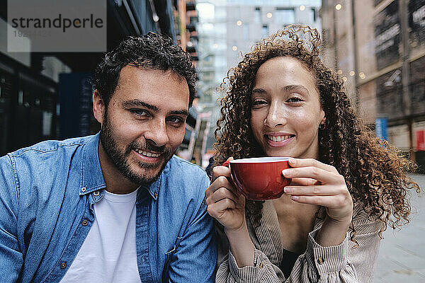 Glücklicher Mann und Frau halten Kaffeetasse im Straßencafé