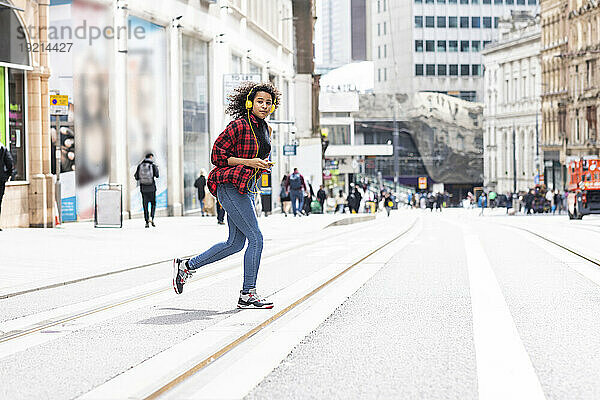 Young woman wearing headphones and crossing street in city