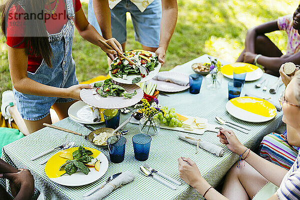 Friends serving food at picnic table in garden