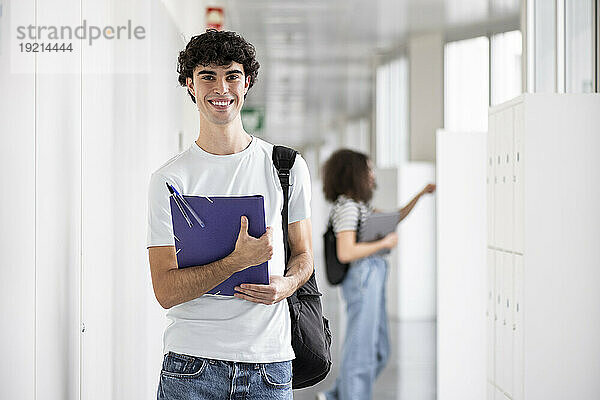 Happy student holding file folder and standing in corridor
